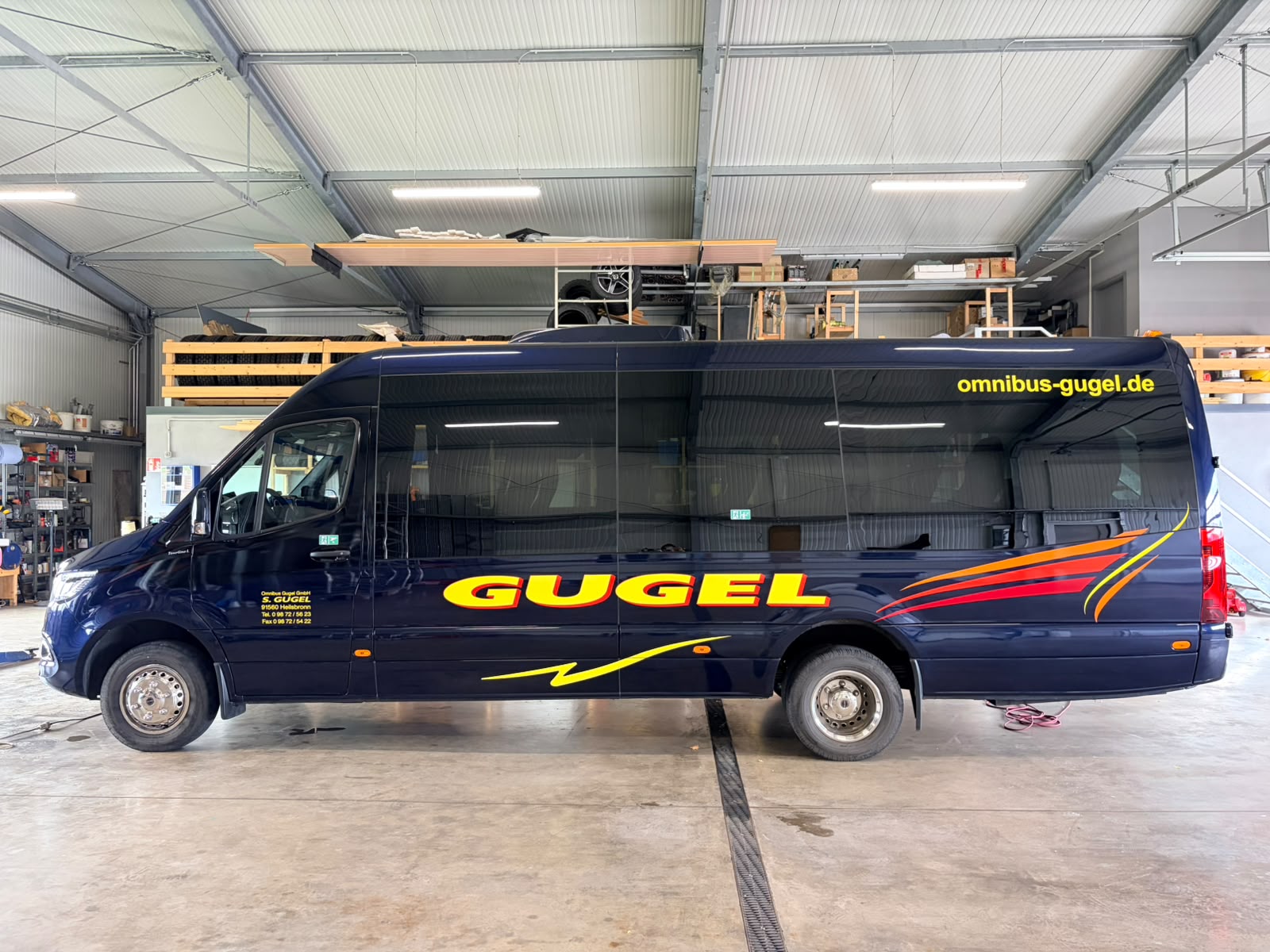 Dunkelblauer Gugel-Kleinbus mit gelbem Schriftzug und rot-orangefarbenen Designelementen auf der linken Fahrzeugseite