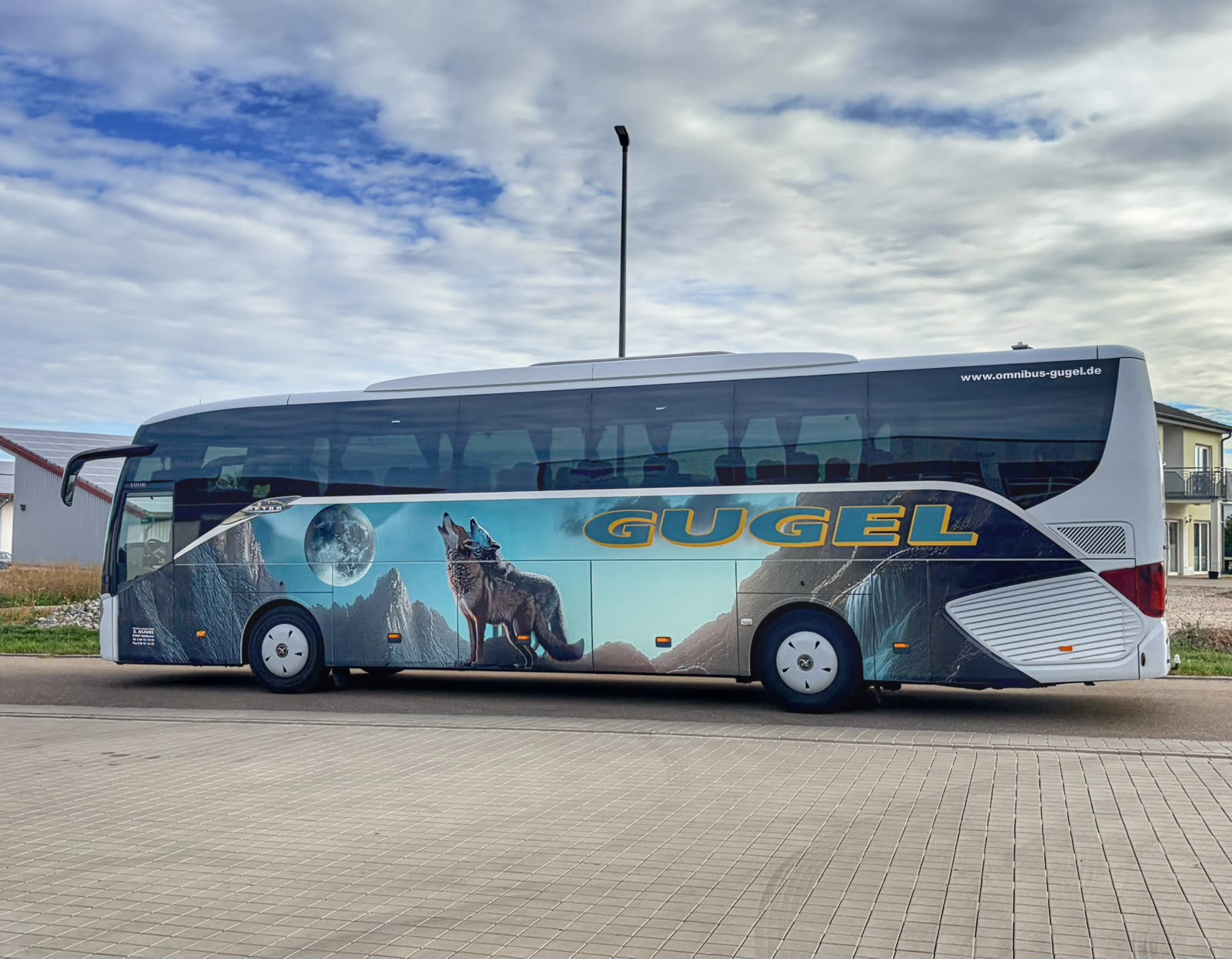 Weißer Gugel-Reisebus mit großflächigem Wolfsmotiv, Mond und Berglandschaft in der Seitenansicht
